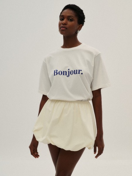 Λευκή κοντομάνικη βαμβακερή oversized μπλούζα, σε ίσια γραμμή, με κλειστή στρογγυλή λαιμόκοψη, ρεγκλάν μανικοκόλληση και μπλε λογότυπο "Bonjour" Combos Knitwear 