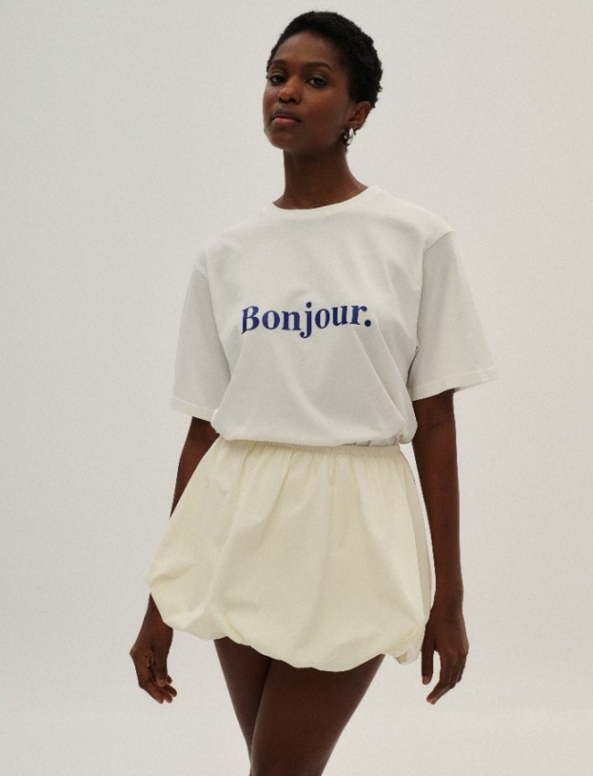 Λευκή κοντομάνικη βαμβακερή oversized μπλούζα, σε ίσια γραμμή, με κλειστή στρογγυλή λαιμόκοψη, ρεγκλάν μανικοκόλληση και μπλε λογότυπο "Bonjour" Combos Knitwear 