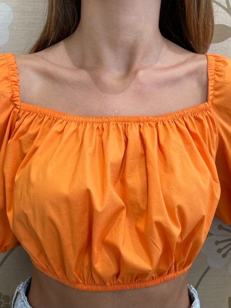 Πορτοκαλί κοντομάνικη βαμβακερή cropped μπλούζα με έξω ώμους, λάστιχο στα τελειώματα και δέσιμο με κόμπο στην πλάτη We coss