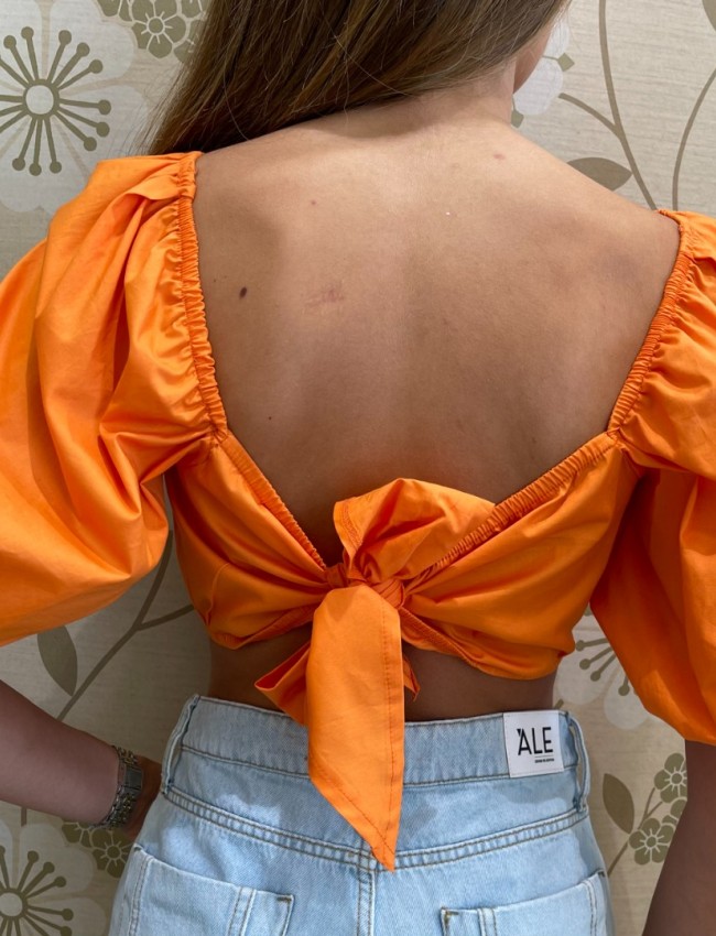 Πορτοκαλί κοντομάνικη βαμβακερή cropped μπλούζα με έξω ώμους, λάστιχο στα τελειώματα και δέσιμο με κόμπο στην πλάτη We coss
