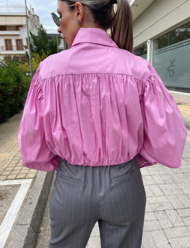 Ροζ μακρυμάνικο ποπλίνα cropped πουκάμισο με πολλές πιέτες-σούρες, έντονα φαρδιά μανίκια, κλείσιμο με ιδιαίτερο κουμπί στην λαιμόκοψη και στις μανσέτες We coss