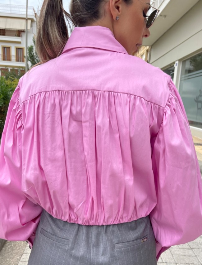 Ροζ μακρυμάνικο ποπλίνα cropped πουκάμισο με πολλές πιέτες-σούρες, έντονα φαρδιά μανίκια, κλείσιμο με ιδιαίτερο κουμπί στην λαιμόκοψη και στις μανσέτες We coss