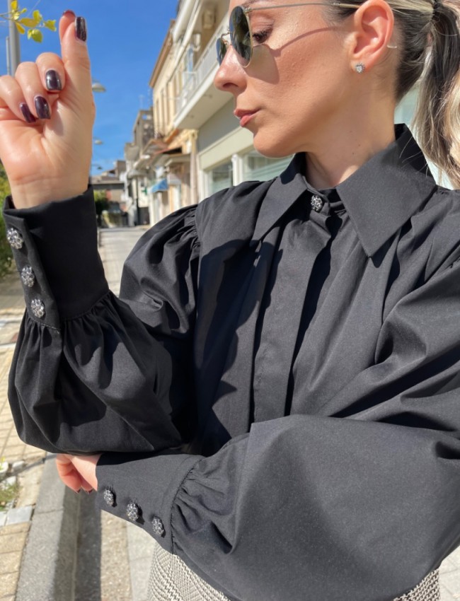 Μαύρο μακρυμάνικο ποπλίνα cropped πουκάμισο με πολλές πιέτες-σούρες, έντονα φαρδιά μανίκια, κλείσιμο με ιδιαίτερο κουμπί στην λαιμόκοψη και στις μανσέτες We coss