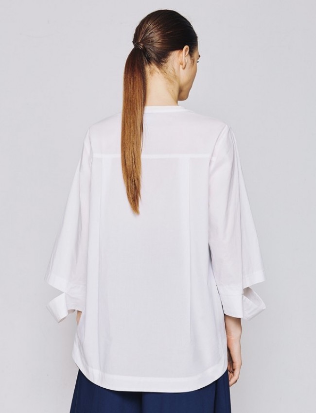 Λευκή μακρυμάνικη oversized μπλούζα με χαμόγελο λαιμόκοψη, συνδυασμό υφασμάτων από ποπλίνα στο πίσω μέρος με διπλή πιέτα, ιδιαίτερο άνοιγμα στις μανσέτες και ασύμμετρο τελείωμα access 
