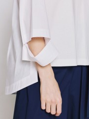 Λευκή μακρυμάνικη oversized μπλούζα με χαμόγελο λαιμόκοψη, συνδυασμό υφασμάτων από ποπλίνα στο πίσω μέρος με διπλή πιέτα, ιδιαίτερο άνοιγμα στις μανσέτες και ασύμμετρο τελείωμα access 