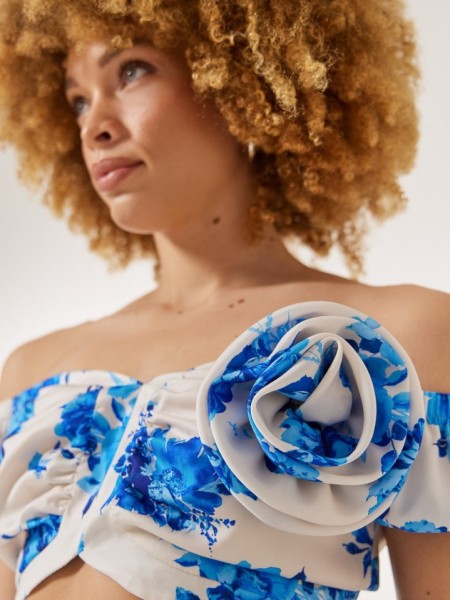 Floral printed γαλάζια κοντομάνικη cropped μπλούζα, με λάστιχο στους έξω ώμους, σούρες στο μπούστο και κλείσιμο με χρυσό φερμουάρ πίσω Enzzo 